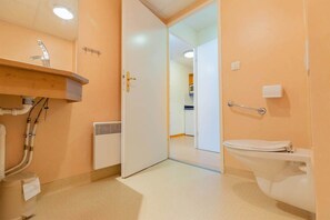 Kylpyhuoneessa on valkoinen pesuallas, wc ja ovi, joka johtaa toiseen huoneeseen.