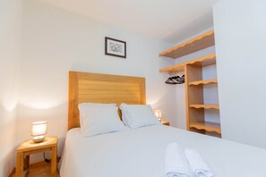 Ein ordentlich bezogenes Bett mit weißen Leinentüchern, einem Holz-Kopfende und einer Nachttischlampe.
