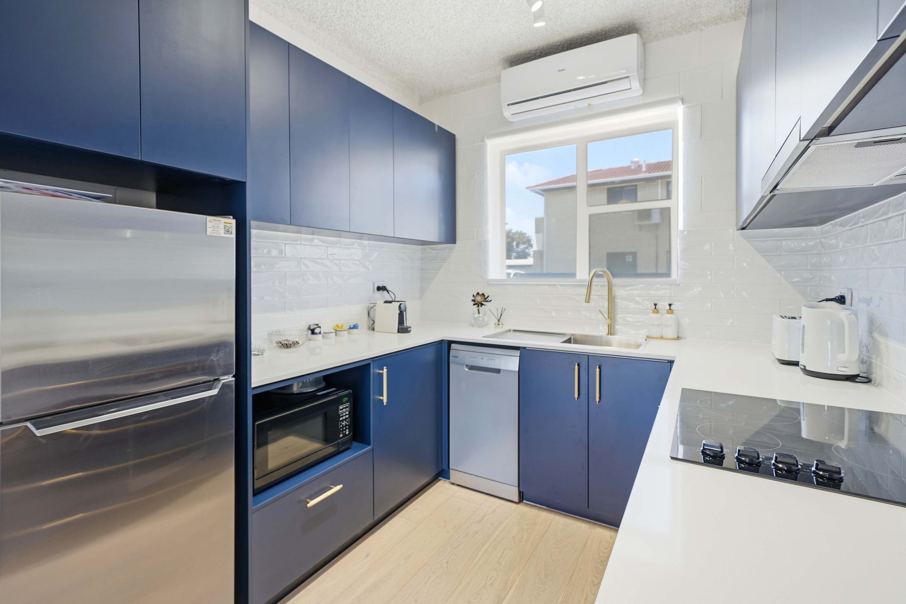 Una cocina moderna con electrodomésticos de acero inoxidable, armarios azules y un ventanal que aporta luz natural.