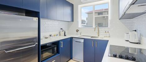 Una cocina moderna con electrodomésticos de acero inoxidable, armarios azules y un ventanal que aporta luz natural.