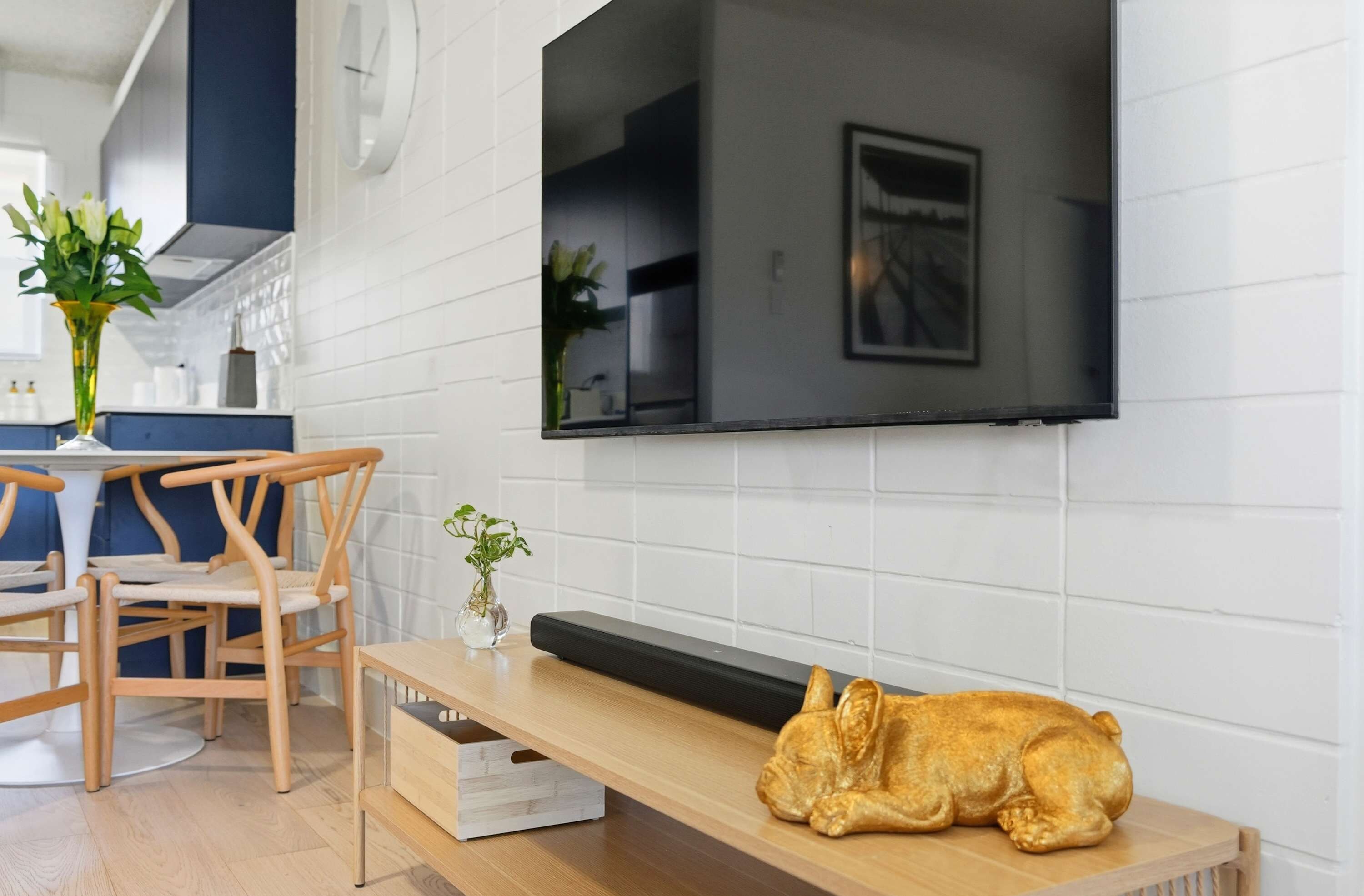 Una sala moderna con un televisor de pantalla plana montado en la pared, un banco de madera y una pequeña mesa con un jarrón de flores.