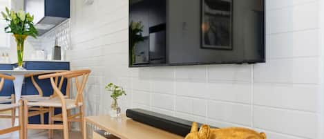 Una sala moderna con un televisor de pantalla plana montado en la pared, un banco de madera y una pequeña mesa con un jarrón de flores.