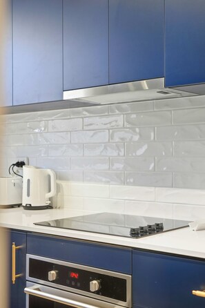 A kitchen with a stainless steel range hood, a white tiled backsplash, and a digital clock displaying 13:42. - Driftwood at West Beach - Steps to Sand & Sailing (West Beach)