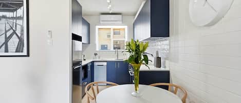 Une cuisine moderne avec des meubles de couleur bleu foncé, un pare-feu en carreaux blancs et une table de salle à manger ronde entourée de chaises en osier.