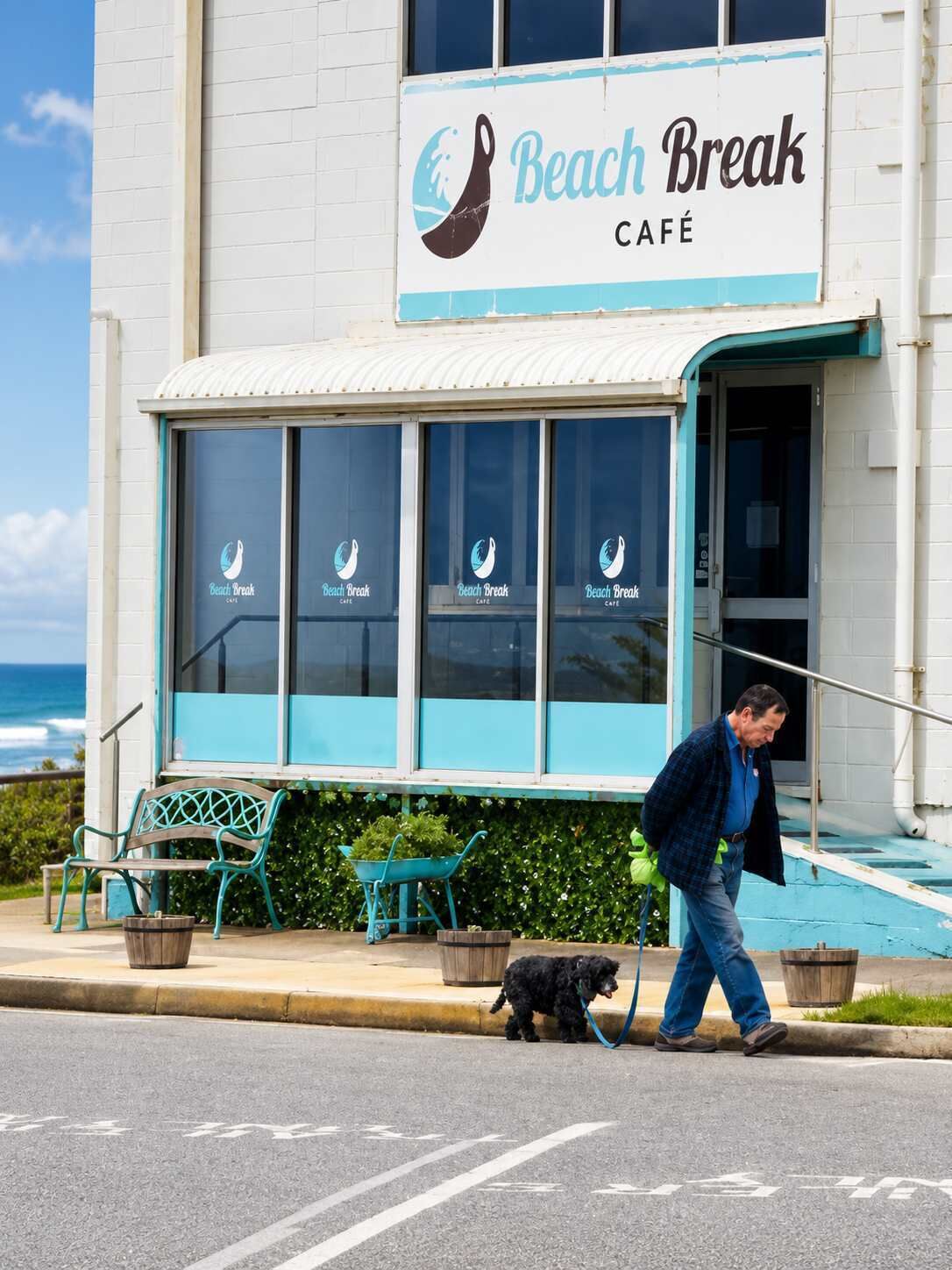 A café with a sign reading 'Beach Break Café' and a dog walking on the sidewalk.