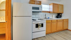 Une cuisine compacte équipée d’un réfrigérateur, d’une cuisinière, d’un four à micro-ondes et de meubles de rangement en bois.