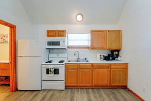 A compact kitchen with white appliances, wooden cabinets, and a window.