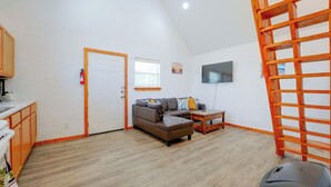 Un vaste espace de vie comprenant un canapé, une table basse, un téléviseur fixé au mur et une échelle en bois.