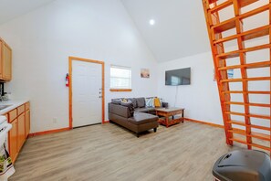 Amplia sala de estar con sofá, mesa de centro, televisor montado en la pared y escalera de madera.