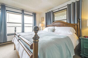 A bedroom with a wooden bed, a nightstand, a lamp, and a window with curtains. - Bring Your Boat! Grand Lake Escape w/ Dock (Grove)