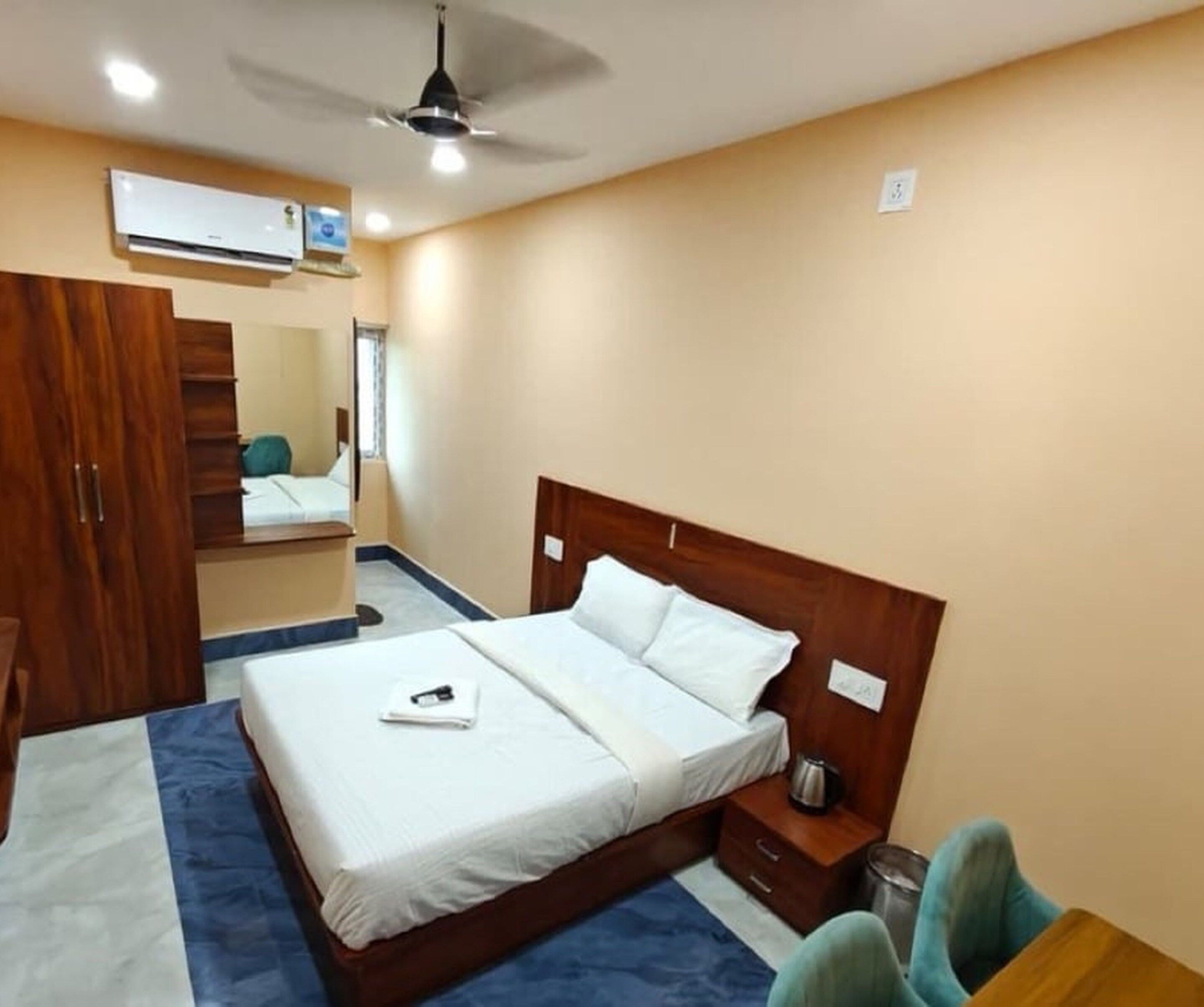 Een hotelkamer met een bed, een houten garderobe, een bureau en een plafondventilator.