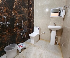 A bathroom with a marble wall, a toilet, a sink, and a shower. - Deluxe Pratikshya & Pratistha (Balianta)