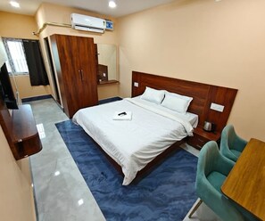 A hotel room with a bed, a desk, a chair, an air conditioner, and a wardrobe. - Deluxe Pratikshya & Pratistha (Balianta)