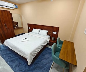 A hotel room with a bed, a desk, a chair, and a wardrobe. - Deluxe Pratikshya & Pratistha (Balianta)
