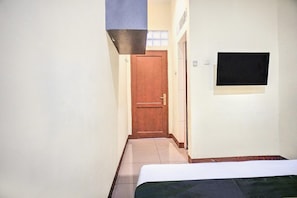 A narrow hallway leading to a door with a small window, a bed with a white mattress, and a black object on the wall. - Cozy Double Escape W/ Free WiFi and Parking (Medan)