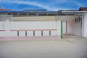A building with a white facade, a red and green door, and a covered area with blue objects. - Cozy Double Escape W/ Free WiFi and Parking (Medan)