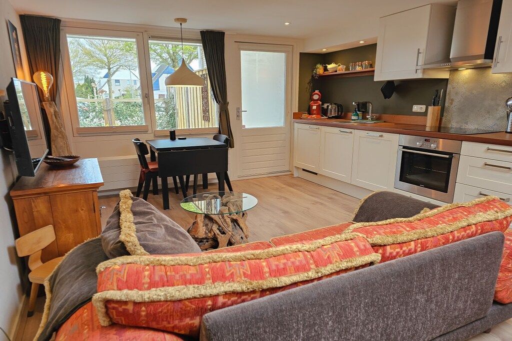 A modern living room with a sofa, a dining table, and a kitchen area with cabinets and appliances.
