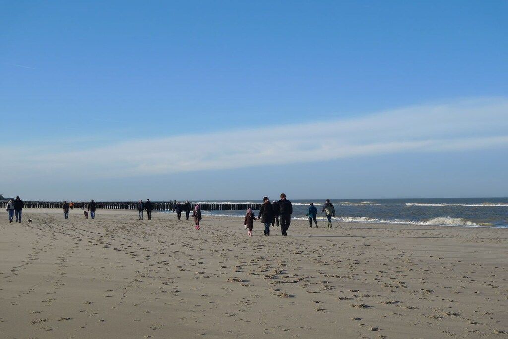 Ein Strand mit Menschen, die am Ufer entlanggehen, und einem Steg, der sich ins Wasser erstreckt.