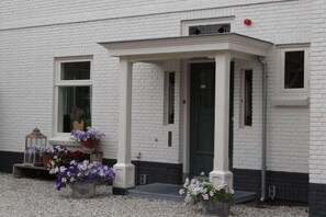A white brick building with a covered entrance, potted plants, and a lantern. - Holiday apartment with 1 bedroom (oostkapelle)