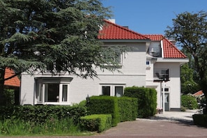 Ein zweigeschossiges Haus mit rotem Ziegeldach, weißen Außenwänden und einem kleinen Balkon im oberen Stockwerk.