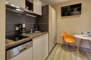 A compact kitchen with a coffee maker, a dishwasher, and a small dining area with a chair and table. - Studio Apartment - Dausch & Gäss-Trög - AD1716 (Marktheidenfeld)