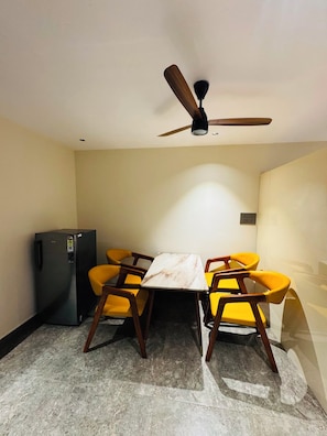 A dining area with a table and four chairs, a ceiling fan, and a refrigerator. - Shreshtam Signature Serviced Apartment (Hyderabad)