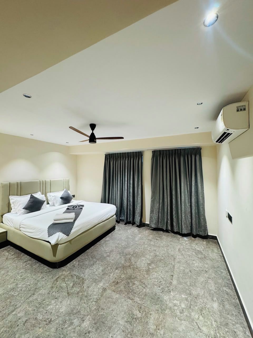 Una habitación de hotel moderna con cama, ventilador de techo y ventana con cortinas.