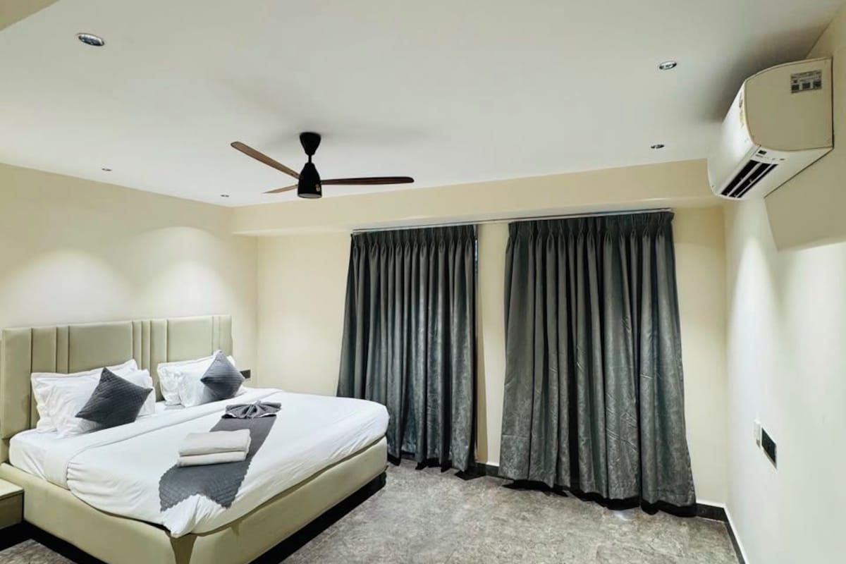 A modern hotel room with a bed, a ceiling fan, and a window with curtains.