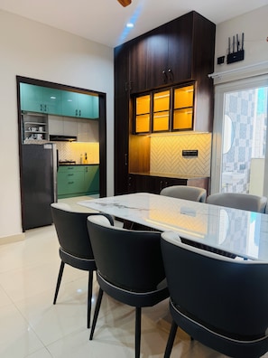 A modern kitchen with dark wood cabinets, a built-in oven, and a dining area with a marble table and black chairs. - Shreshtam Signature Serviced Apartment (Hyderabad)