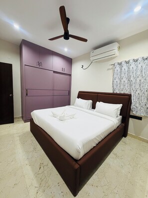 A bedroom with a bed, a ceiling fan, an air conditioning unit, and a wardrobe.