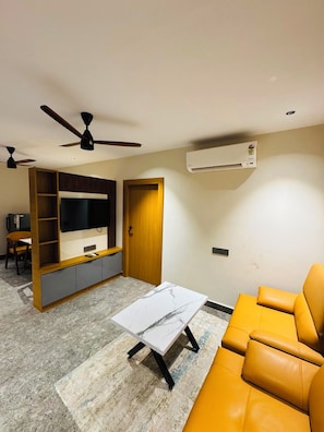 A living room with a sofa, a coffee table, a TV, and a ceiling fan. - Shreshtam Signature Serviced Apartment (Hyderabad)