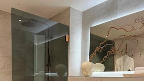 Un baño moderno con ducha envuelta en vidrio, inodoro blanco y tocador oscuro con un espejo arriba.