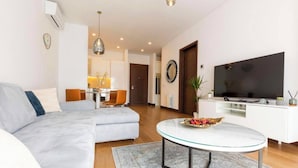 Una sala moderna con un sofá, una mesa de centro de vidrio, un televisor de pantalla plana y un comedor con una mesa y sillas.