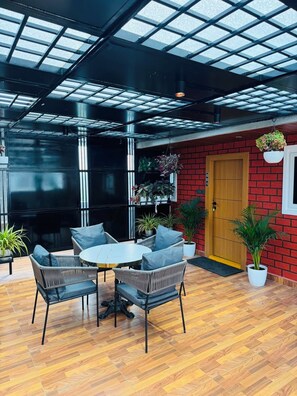 A room with a wooden floor, a round table, and two chairs. There is a red brick wall with a wooden door and a window.