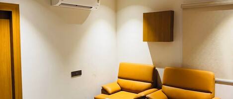 A living room with a sofa, a coffee table, a ceiling fan, and an air conditioning unit.
