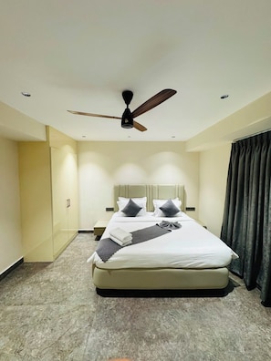 A hotel room with a bed, a ceiling fan, a nightstand, and a glass-enclosed wardrobe. - Shreshtam Signature Serviced Apartment (Hyderabad)