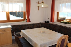 A room with a dining table, a bench, a cross on the wall, and a window with curtains. - Holiday home with 1 bedroom (Hart im Zillertal)