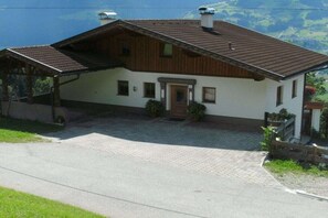 A two-story house with a sloped roof, a front porch, and a paved driveway. - Holiday home with 1 bedroom (Hart im Zillertal)