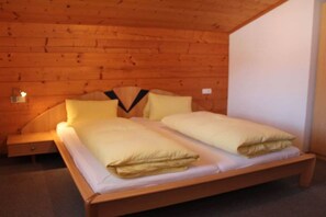 A wooden-paneled room with a bed, a nightstand, and a wall-mounted light. - Holiday home with 1 bedroom (Hart im Zillertal)