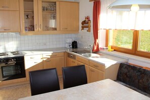 A kitchen with a stove, oven, sink, and dining area with chairs. - Holiday home with 1 bedroom (Hart im Zillertal)