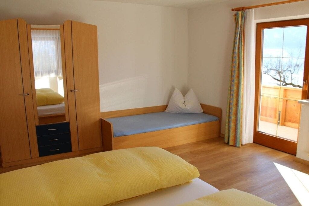 Ein Schlafzimmer mit einem Bett, einer Sitzbank, einem Kleiderschrank und einem Fenster mit Vorhängen.
