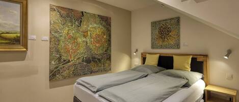 A bedroom with a bed, two bedside tables, and two wall-mounted artworks.