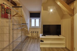 A small room with a TV on a stand, a metal shelf unit, and a wooden bench. - Maisonette Apartment The Haystack AD1716 (Marktheidenfeld)