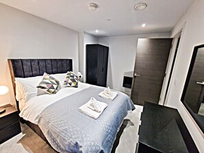 Ein modernes Schlafzimmer mit einem großen Bett, einem Kopfteil, einem Nachttisch und einem Kleiderschrank.