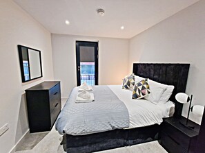Quarto moderno com cama, mesa de cabeceira, cômoda e espelho.
