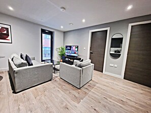 Uma sala de estar moderna com sofás cinza, uma TV de tela plana e uma janela grande.
