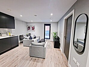Eine moderne Küche mit Flachbildfernseher, ein Essbereich mit Tisch und Stühlen, eine Sitzecke mit Sofa und Sesseln und ein großer Spiegel.