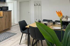 Ein Essbereich mit einem Holztisch, schwarzen Stühlen und einer Pflanze mit orangefarbenen Blüten.