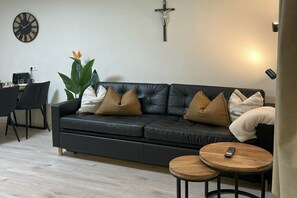 A modern living room with a black leather sofa, two wooden side tables, a coffee table, a potted plant, a wall clock, and a cross. - Holiday apartment with 2 bedrooms (Ried im Zillertal)