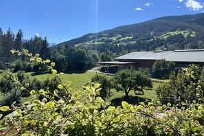 Un edificio con techo inclinado, rodeado de un paisaje verde exuberante y una montaña al fondo.